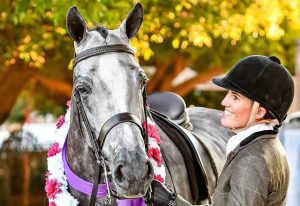 A woman is standing next to a grey horse.