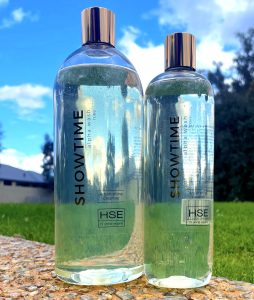Two bottles of HSE Showtime Alpha Wash Shampoo sitting on a grassy area.
