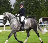 A woman riding a grey horse on a grassy field.