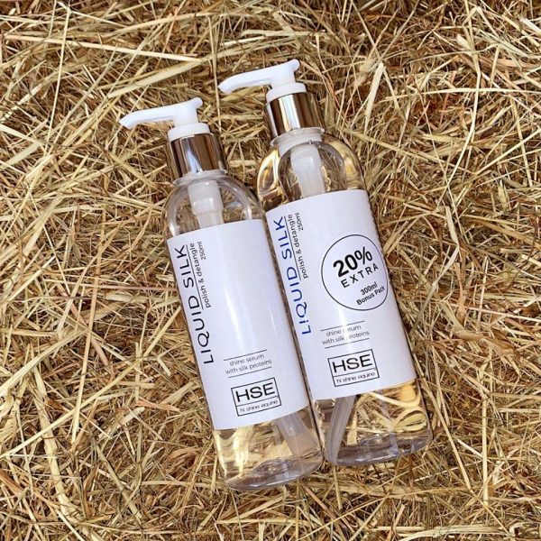 Two bottles of HSE Liquid Silk Hair Polish Serum sitting on hay.
