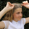 A person secures a beige wig cap over their head in front of a leafy hedge, preparing to adorn an elegant NTR Hairlock.