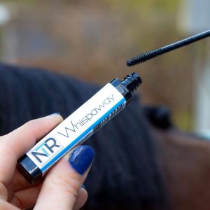 A person holding a tube of mascara next to a horse.