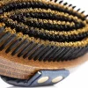 Close-up of the NTR Harmony Copper Brush, a circular wooden brush with dense black and brown bristles and a blue strap with metal buttons.